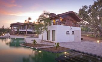 a white building with a balcony and tropical plants is reflected in a pool at sunset at The Serai Bandipur
