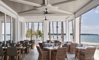 an outdoor dining area with a view of the ocean , featuring a large wooden table surrounded by chairs at Isla Bella Beach Resort & Spa - Florida Keys