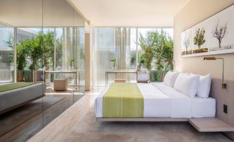 a modern bedroom with a large bed , white walls , and floor - to - ceiling windows overlooking a garden at The Jaffa, a Luxury Collection Hotel, Tel Aviv