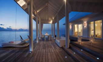 a wooden deck overlooking the ocean at night , with a dining table and chairs set up for a romantic dinner at Diamonds Athuruga Maldives Resort & SPA