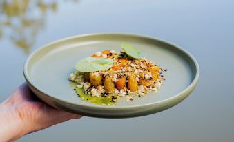 a person is holding a green plate with a dish of food on it , garnished with herbs at Cape Lodge