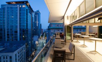 a city rooftop patio with a view of tall buildings and people sitting at tables at The Charter Hotel Seattle, Curio Collection by Hilton