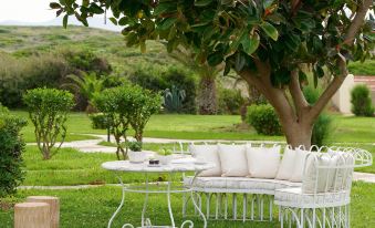 a white couch and table are set up in a garden with a tree and greenery at Grecotel Meli Palace