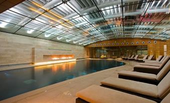 an indoor swimming pool surrounded by a glass ceiling , with several lounge chairs placed around the pool at Lucknam Park Hotel