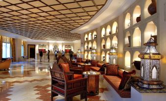 a luxurious hotel lobby with red leather couches , wooden chairs , and a large archway entrance at Djibouti Palace Kempinski