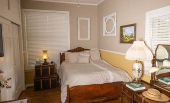 a well - decorated bedroom with wooden furniture , including a bed , nightstand , lamp , and curtains , along with white walls and wooden flooring at Sassafras Inn
