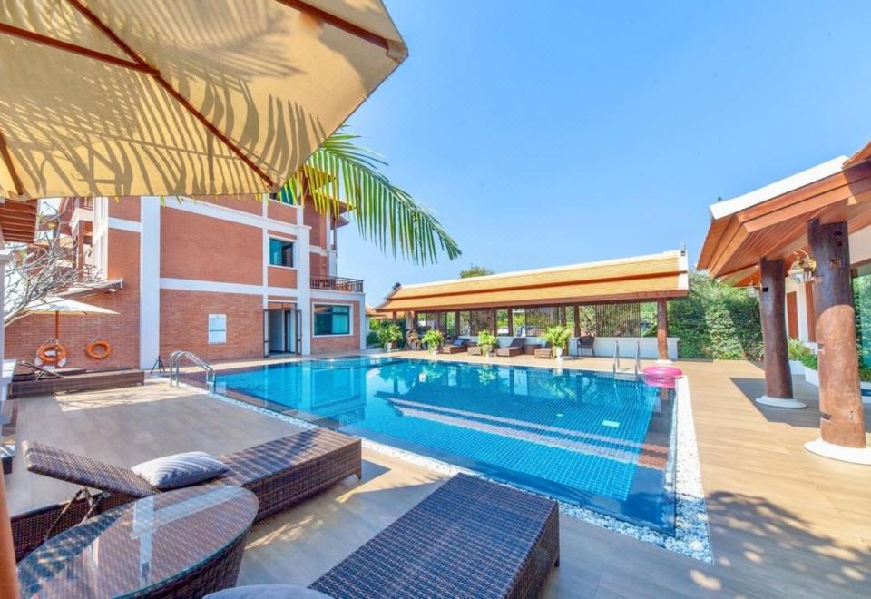 a large swimming pool with lounge chairs and umbrellas is surrounded by a brick building at Content Villa Chiangmai