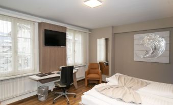 a modern hotel room with wooden floors , white walls , and large windows , featuring a bed , desk , chair , and tv at Hotel Post