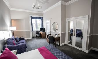 a well - decorated hotel room with a large bed , purple couch , and white dresser , along with a tv and dining table at Kincaid House Hotel