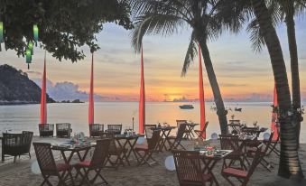 a beachfront restaurant with umbrellas and tables set up , overlooking the ocean at sunset at Anantara Rasananda Koh Phangan Villas