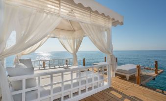 a white gazebo with a canopy overlooks the ocean from a wooden deck , providing a serene and relaxing atmosphere at Titanic Deluxe Lara