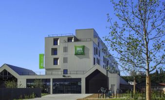 a modern hotel building with a green sign and a bicycle parked in front , under a clear blue sky at Ibis Styles Paris Romainville