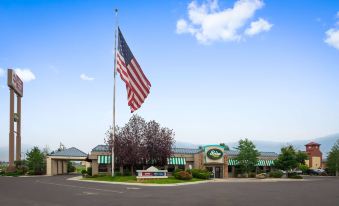 a large american flag flying high in the sky , with a building and some trees in the background at Best Western Plus Butte Plaza Inn