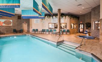 an indoor swimming pool with a diving board , surrounded by chairs and tables , and under hanging decorations at Best Western Plus Butte Plaza Inn