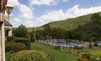 a large swimming pool is surrounded by a garden with benches and greenery , overlooking a mountainous landscape at Bestbrook Mountain Farmstay