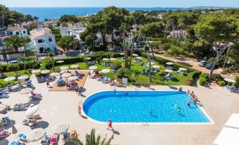 a resort with a large swimming pool surrounded by palm trees and people enjoying the water at Globales Cala Blanca