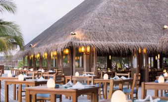 a dining area with several tables and chairs , some of which are set up under thatched roof at Meeru Maldives Resort Island
