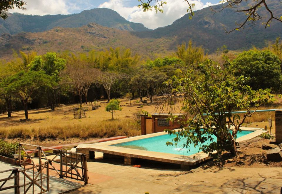 a large outdoor swimming pool surrounded by a wooden deck , with mountains in the background at Jungle Hut