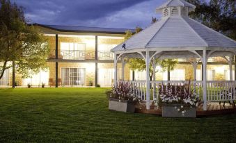 a beautiful white gazebo in a grassy yard , with flowers and greenery surrounding it during the evening at Parklands Resort Mudgee