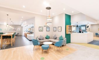 a modern , minimalist lounge area with wooden floors and green walls , featuring comfortable seating arrangements and a bar at Holiday Inn Gloucester - Cheltenham