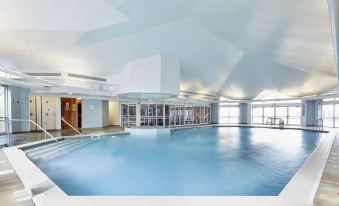 a large , modern swimming pool with a white interior and blue water is surrounded by glass walls and large windows at Coldra Court Hotel by Celtic Manor
