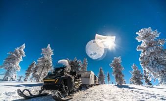 a snowmobile is driving on a snowy road with a full moon in the sky at Northern Lights Village