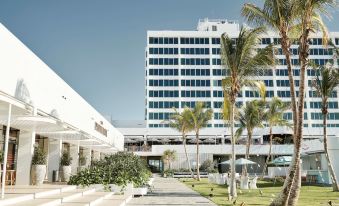 a large white building with a tall tower is surrounded by palm trees and covered walkways at The Ville Resort - Casino