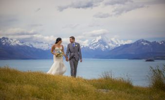 a bride and groom standing on a grassy hill , holding hands , with a beautiful mountainous landscape in the background at Lakestone Lodge