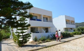 a group of people walking in front of a white building with balconies and a garden at Aphrodite Beach Hotel