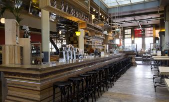 a long wooden bar with stools and a row of bottles behind it , under a skylight at Hotel New York