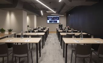 a conference room with rows of tables and chairs , a screen displaying a video , and a microphone at Moxy Patra Marina