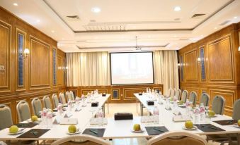 a conference room with a long table and chairs arranged for a meeting , with a projector screen on the wall at Marigold Hotel