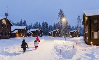 a group of people , including children , are playing in the snow near a row of wooden cabins at Ranua Resort Holiday Villas