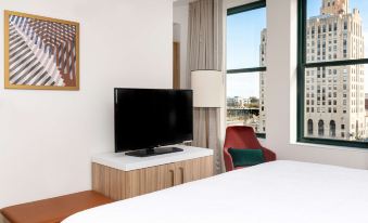 a hotel room with a large flat - screen tv mounted on the wall above a wooden bed at Hilton Garden Inn Flint Downtown
