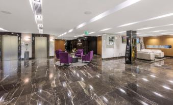 a spacious and well - lit hotel lobby with purple chairs , marble floors , and a green exit sign at Meriton Suites North Ryde