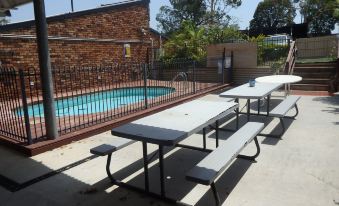 a set of picnic tables and benches in an outdoor setting with a pool visible at Kallangur Motel