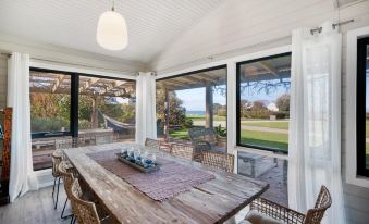 a wooden dining table surrounded by chairs , situated in a room with a view of the ocean at Bear Gully Coastal Cottages