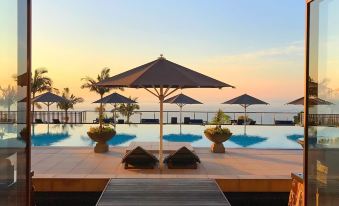 a wooden deck overlooks a pool with an umbrella and palm trees , set against the backdrop of a serene ocean and sky at Sankara Hotel & Spa Yakushima