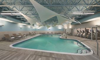 an indoor swimming pool surrounded by lounge chairs and a ceiling made of white beams at Courtyard Oshawa