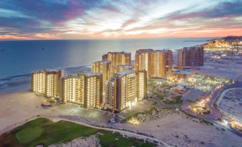 an aerial view of a large , modern apartment complex near the ocean at sunset , with multiple floors of buildings and illuminated by lights at Las Palomas Beach & Golf Resort