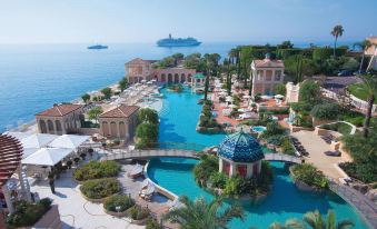a large resort with a pool and a cruise ship in the background , surrounded by palm trees and other tropical vegetation at Monte-Carlo Bay Hotel & Resort