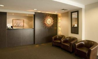 a modern office lobby with a brown leather couch , chairs , and a large sun mirror on the wall at St Ives Apartments