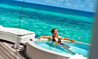 a woman relaxing in a hot tub on a wooden deck , surrounded by clear blue water at Diamonds Athuruga Maldives Resort & SPA