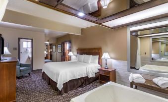 a large bed with a wooden headboard and white linens is in the middle of a room with a bathtub at Best Western Dunmar Inn