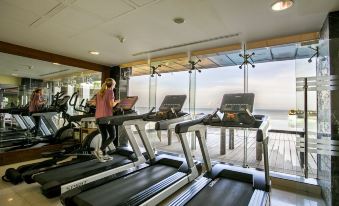 A woman is exercising on a treadmill in a spacious indoor gym with large windows at Sayeman Beach Resort