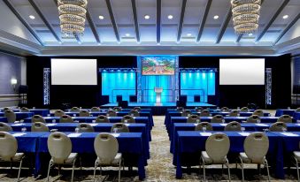 a conference room with blue chairs and tables , a large screen on the wall , and chandeliers hanging from the ceiling at The Grand Hotel Golf Resort & Spa, Autograph Collection