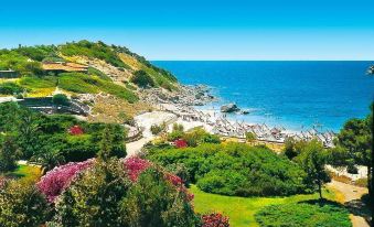 a picturesque coastal landscape with a pathway winding through the greenery , leading to the ocean at Falkensteiner Resort Capo Boi