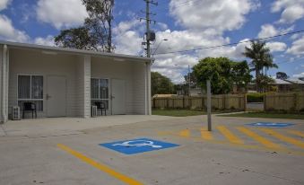 a white building with a blue parking area and an electrical box in front of it at Kallangur Motel