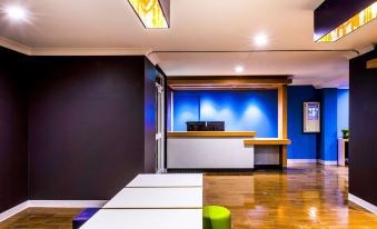 a hotel lobby with a wooden floor , a reception desk , and several chairs arranged around it at ibis budget Casula Liverpool