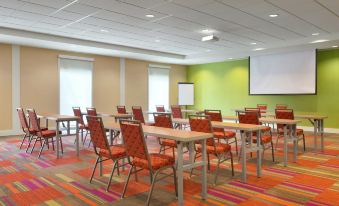 a large conference room with multiple rows of chairs arranged in a semicircle , and a projector screen mounted on the wall at Home2 Suites by HIlton Cartersville